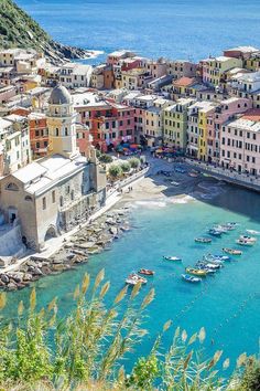 boats are docked in the blue water next to colorful buildings and cliffs on the shore