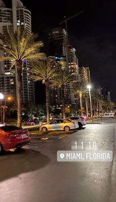 a city street at night with cars parked on the side and palm trees in the foreground