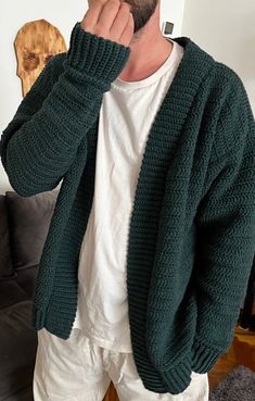 a man standing in front of a mirror wearing a green cardigan sweater and white pants