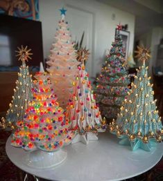 three small christmas trees on a table with other ornaments in the background and one is made out of plastic