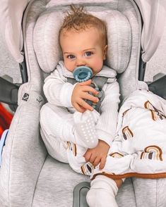 a baby sitting in a stroller holding a pacifier