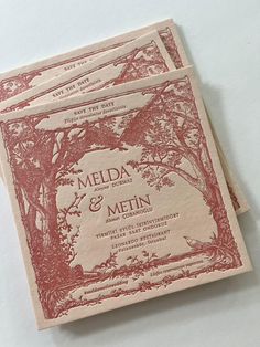 two red and white wedding cards sitting on top of each other with trees in the background