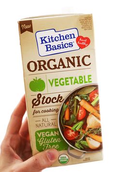 a person holding up a box of organic vegetable stock in front of a white background