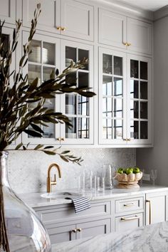 a kitchen with white cabinets and marble counter tops, gold accents on the doors and drawers