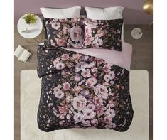 a bed with pink and black floral comforter set on top of a white rug