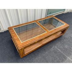 a wooden coffee table with glass doors on the top and bottom, in front of a building