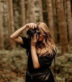 a woman is standing in the woods with a camera