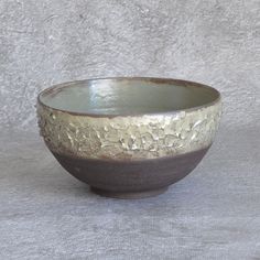 a brown and white bowl sitting on top of a gray cloth covered table next to a wall