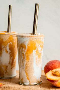 two glasses filled with ice cream and peaches next to an apple on a wooden table