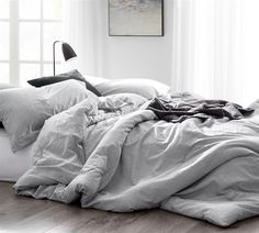 an unmade bed with white sheets and pillows in a room next to a window