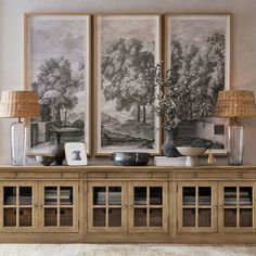 two framed pictures on the wall above a wooden cabinet with glass doors and drawers underneath