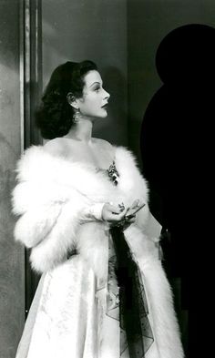 a black and white photo of a woman in a fur coat standing next to a man