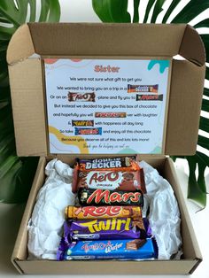 an open box filled with assorted chocolates and other candy bar items next to a potted plant