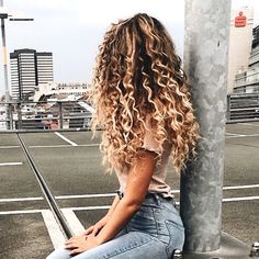 a woman sitting on top of a metal pole next to a street light with her hair blowing in the wind