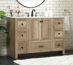 a bathroom vanity with wooden drawers and a round mirror above it, in front of a white brick wall