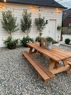 a wooden picnic table sitting in front of a white house with potted plants on it