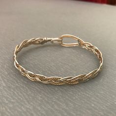 These bracelets are braided using a standard three-strand pattern, just like you would use when braiding hair or rope. The large hook and eye closure is part of the entire design, and allow the wearer to hook and unhook the bracelet with one hand; no helper should be needed! I have two variants: silver with a twisted gold wire as an accent and gold with a twisted silver wire. I make them in a range of sizes (in 1/4 inch increments) to fit any wrist. Yes! Sizes!! To determine the size you need, m Wire Jewelry Closures, Twisted Wire Bracelet, Braided Wire Bracelet, Adjustable Metal Jubilee Braided Bracelets, Adjustable Bracelet With A Modern Twist, Adjustable Metal Bangle With A Modern Twist, Adjustable Gold Braided Bracelet Hand Wrapped, Adjustable Bangle With A Modern Twist, Adjustable Metal Braided Bangle Bracelet