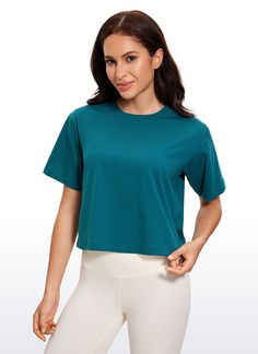 a woman in white pants and a teal top is posing for the camera with her hands on her hips