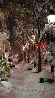 a snowy city street at night with christmas decorations on the trees and lights in the snow