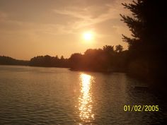 the sun is setting over some water and trees