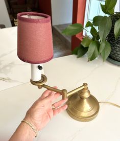 a person holding a lamp on top of a white table next to a potted plant