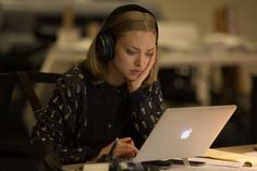 a woman sitting at a desk with headphones on and looking at her laptop computer