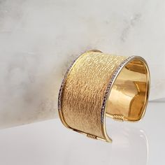 Introducing our exquisite 18K Gold-Plated Textured Cuff Bracelet, a true embodiment of sophistication and style. This unique piece features a captivating texture, adding a touch of allure to your wrist. The brilliance of 18K gold plating enhances the luxurious appeal, while a meticulously crafted silver frame beautifully complements the textured design. This combination of gold and silver elements creates a striking visual contrast, making the bracelet a statement accessory. Designed with attent Elegant Diamond Cut Cuff Bracelet For Anniversary, Luxury Bangle With Elegant Design For Anniversary, Elegant Open Cuff Bracelets For Party, Fine Jewelry Bangle Cuff Bracelet For Formal Occasions, Luxury Gold Cuff Bracelets, Modern Gold Bangle For Formal Occasions, Luxury Cuff Bracelet Bangle For Anniversary, Luxury Cuff Bangle Bracelet For Party, Luxury Cuff Bracelets For Anniversary