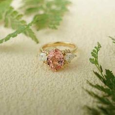 a pink ring sitting on top of a white surface next to green leafy branches