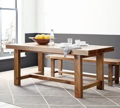 a wooden table with two benches and a bowl of fruit on it in front of a window