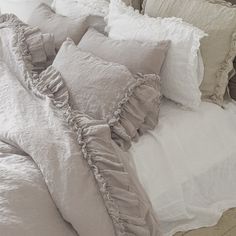 a bed with white sheets and ruffled pillows