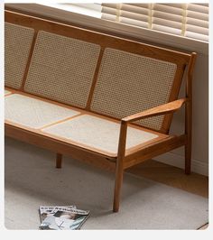 a wooden bench sitting in front of a window next to a magazine on the floor