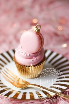 a pink frosted cupcake sitting on top of a gold plate next to a fork