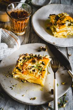 a piece of quiche on a plate next to a glass of tea and a fork