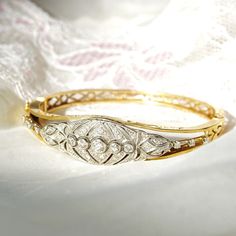 An astounding Edwardian era diamond cluster hinge bangle bracelet in 14k yellow gold and platinum. Features an ornate diamond-encrusted platinum navette setting mounted on a tapered gold band with cutout embellishments and a latch box clasp. Built into the focal point of this bracelet is 5 round-cut diamonds secured in a horizontal line of bezel settings. The open work on either side of the platinum setting is also decorated with three prong-set diamond accents. All the diamonds seem to be in go Antique Round Cuff Bracelet For Wedding, Wedding Bangle In Yellow Gold With Brilliant Cut, Wedding Brilliant Cut Yellow Gold Bangle, Wedding Yellow Gold Bangle With Brilliant Cut, Antique 14k Gold Bangle For Anniversary, Formal Diamond Cuff Bracelet Fine Jewelry, Classic Hallmarked Cuff Bracelet For Wedding, Fine Jewelry Anniversary Bracelet With Rose Cut Diamonds, Classic Wedding Bangle Hallmarked