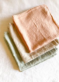 three folded towels sitting on top of a white tablecloth next to each other in different colors