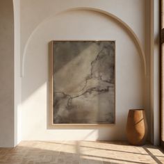 an abstract painting hangs on the wall next to a vase and window in a white walled room