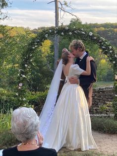 a bride and groom kissing in front of an arch with flowers on the ground behind them