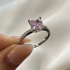 a person holding a ring with a pink diamond in the middle and white diamonds around it