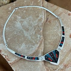 This gorgeous Sterling Silver Necklace, as part of the Red Moon collection, features Black Jade, Kingman Turquoise and Blue, Blue/Green & Red Lab Opal Dimensions: Center Link 1 3/4"W x 1 1/8"H; Total Length of Sterling Silver/Inlaid Links: 9"; Total Length of Necklace: 17" They are designed by David Rosales, one of the finest contemporary Southwest Artists in the world. He is the founder and co-owner of Supersmiths, Inc. of Gallup, NM. This Handcrafted Necklace is custom made and carries a lifet Artisan Red Jewelry With Inlay, Artisan Red Inlay Jewelry, Red Sterling Silver Jewelry With Inlay, Blue Necklace With Round Inlay, Collectible Blue Inlay Necklace, Artisan Red Collectible Necklaces, Artisan Red Jewelry With Large Pendant, Red Southwestern Sterling Silver Necklace, Artisan Red Round Pendant Jewelry