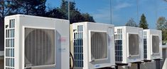 three air conditioners lined up on the side of a building with trees in the background