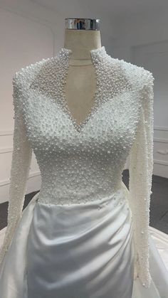 a white wedding dress with beading on the neck and sleeves, is displayed in front of a mannequin