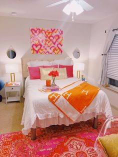 a white bed with orange and pink decor in a bright colored bedroom, along with two lamps on either side of the bed