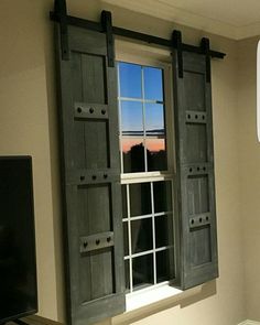 an open window with wooden shutters in a living room next to a flat screen tv