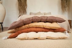 four pillows stacked on top of each other in front of a white vase with hay behind it