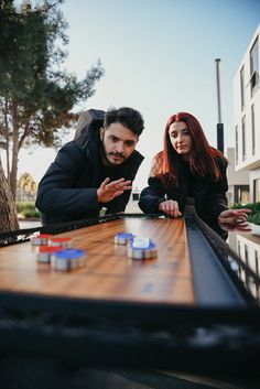 a man and woman playing board games on a wooden table in front of a building