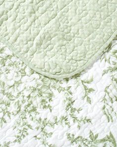 an unmade bed with green and white floral bedspread on top of it