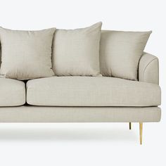 a beige couch with four pillows on it's back and two arms, in front of a white background