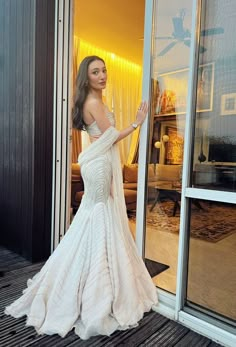 a woman in a white dress standing on a wooden floor next to a glass door