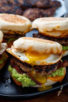 three burgers with eggs, bacon and guacamole on a black plate