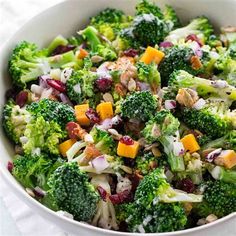 a bowl filled with broccoli, cranberries and other vegetables on top of a white cloth